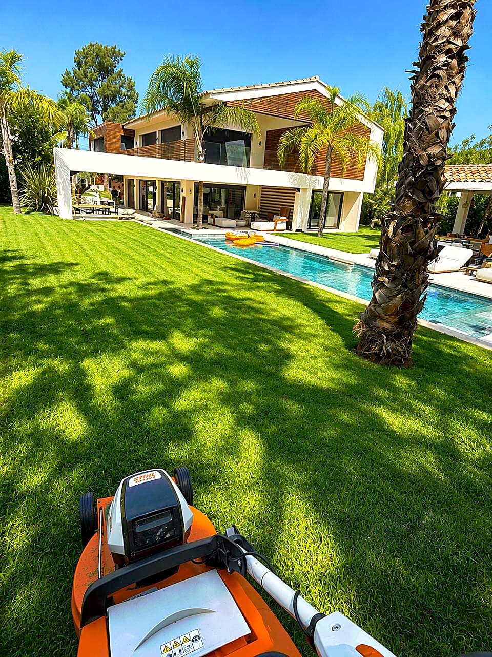 Pelouse fraîchement tondue devant une villa et sa piscine
