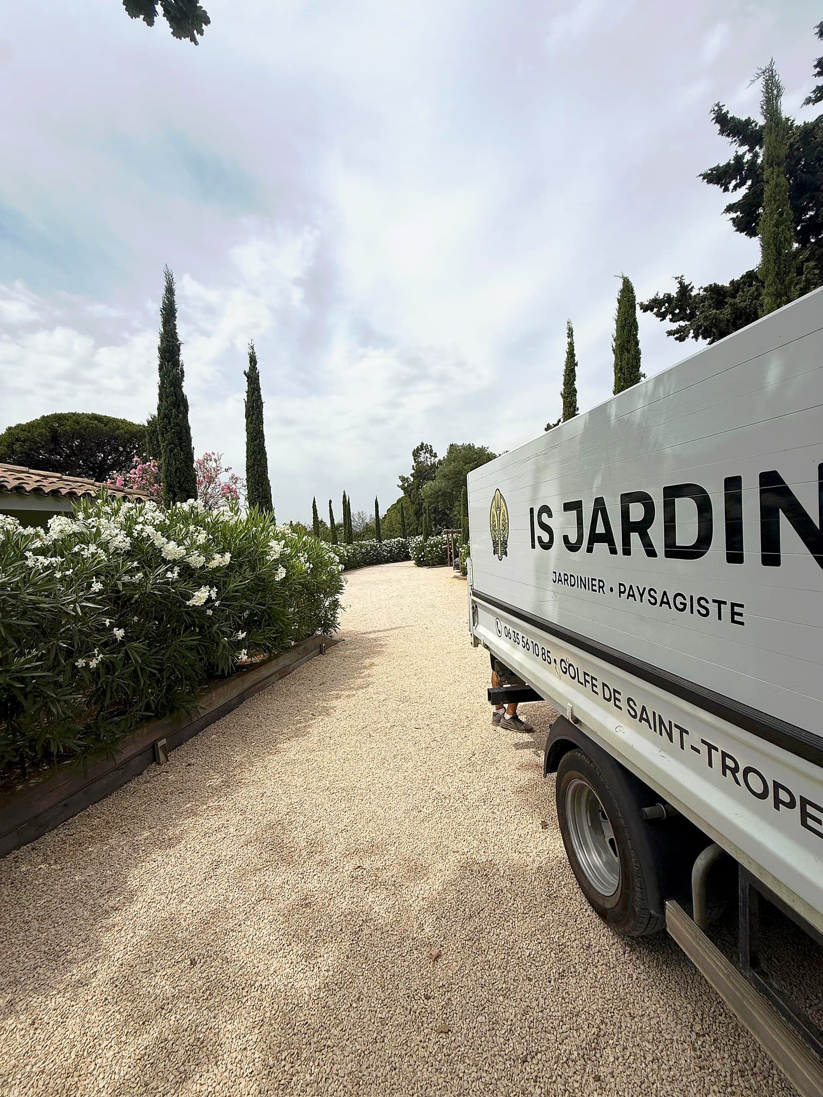 Camion IS JARDIN sur une allée de gravier bordée de cyprès et de lauriers